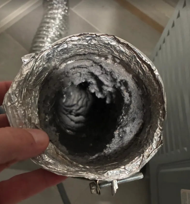 A cut section of flex duct with its opening choked down by packed lint
