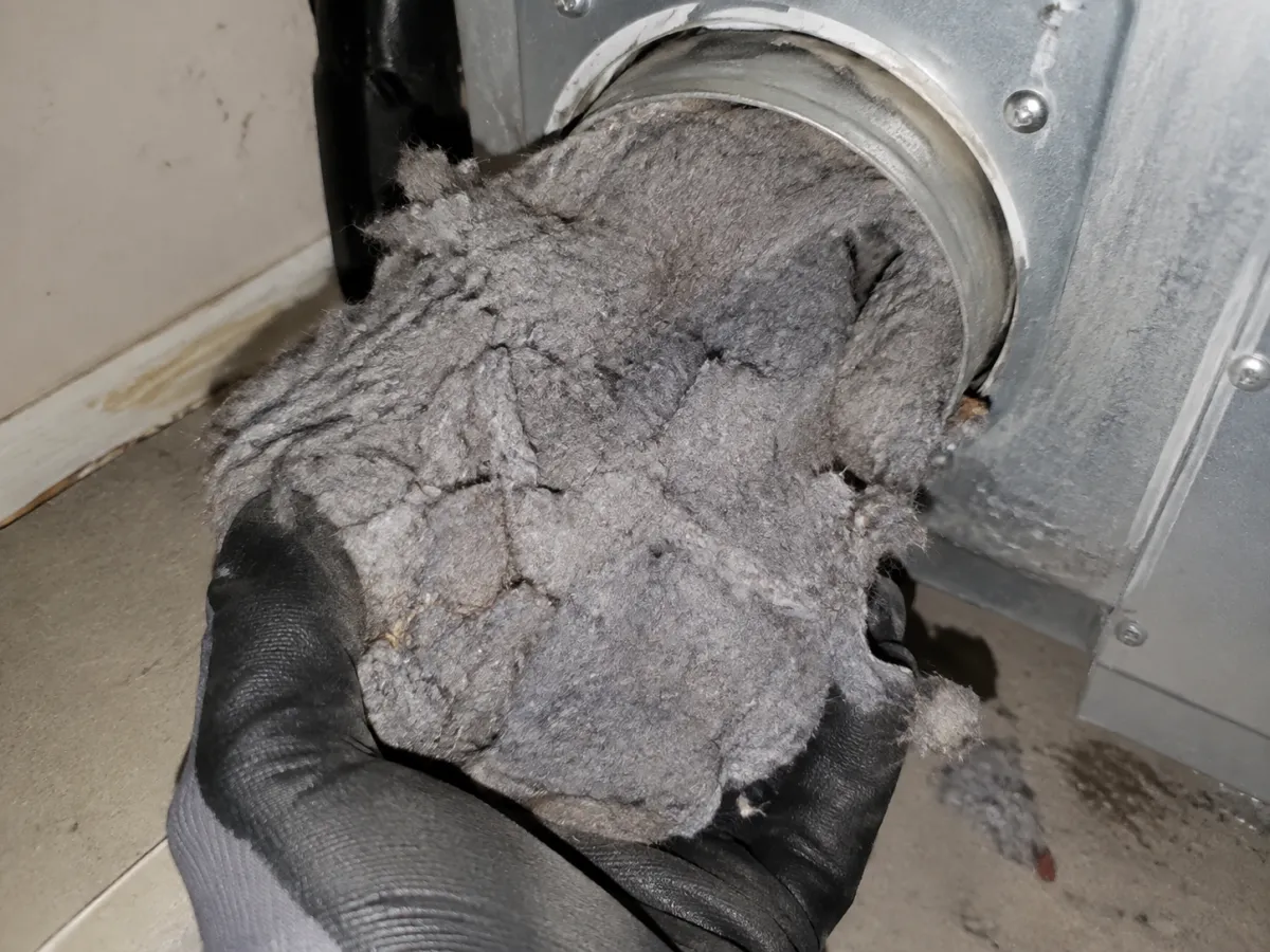 A handful of compacted lint at a dryer duct opening